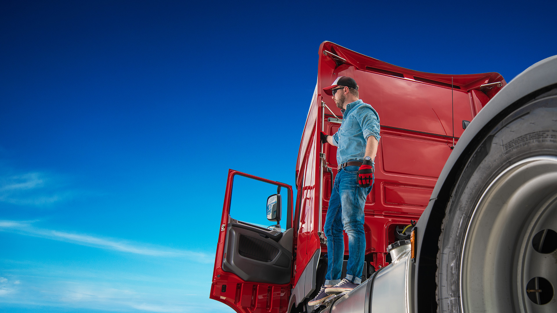 Against the background of the blue sky stands a tractor with an open driver&#39;s door, a TIR driver in a hat and glasses probably stands on the tractor platform.